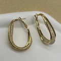 Close-up of golden U-shaped hoop earrings with intricate inner grid texture and polished finish - Gold Oval Style