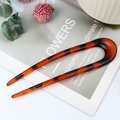 U-shaped hair pin in leopard tortoiseshell finish placed on a magazine for daily bun styling - Red Leopard Print