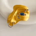 Macro view of surrealist face brooch with yellow enamel finish and blue eyeball detail - Gold