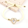 Dettaglio del braccialetto in corda gialla intrecciata con ciondolo a cuore e malocchio - Bianco