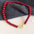 Vista macro di una collana di perle rosso scuro con fibbia dorata e zirconi micro-incastonati - Rosso
