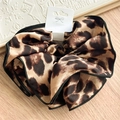 Close-up of leopard print satin scrunchie with black edging on a wooden surface - Black Edged Style / Black Edged Leopard