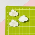 Detailed view of three cloud-shaped resin charms in white and translucent texture on a mat - 5# White