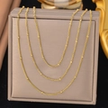 Detailed macro view of triple layered golden beaded chain necklaces on a jewelry display - Three-layer Satellite Round Bead Chain (QZXLH1277) / Gold