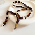 Dettaglio della collana boho in tessuto con perline in legno e resina su piatto bianco - Stile Patchwork a Righe