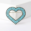 Detalle de un broche corazón de bronce vintage con cuentas azules sobre fondo blanco - Azul