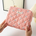 Close-up of red plaid quilted makeup bag with blue bow details and brand label - Medium / Red Grid with Bow