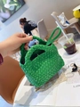 Close-up of a green hand-woven mini bucket bag held in a bright cafe setting - Green