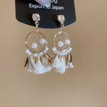 Détail de boucles d'oreilles bohèmes avec pompons, perles, cristaux et feuilles dorées - Or / Doré