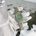 Close-up of women's emerald tonneau watch with diamond accents on a reflective water surface - Two-tone Green Dial