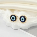 Detalle de pendientes de ojo turco de resina azul con borde dorado sobre seda blanca - Ojo Azul Dorado