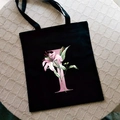 Black canvas tote bag featuring a pink letter T and lily flower print with dual handles - Letter I / Black