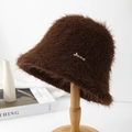 Detail view of brown plush faux fur bucket hat with metal letter plaque on a wooden stand - Coffee