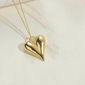 Makroaufnahme eines 3D-Herzanhängers an einer Goldkette auf strukturiertem Steinboden - Großes Herz / 14K Gold