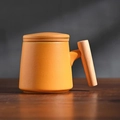 Matte orange ceramic tea mug with wooden handle and lid on a dark wood surface - Orange