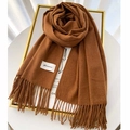 Close-up of caramel cashmere scarf texture with hand-knotted tassels and brand label - Caramel color