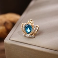 Dettaglio macro di elegante spilla a corona dorata con pietra blu a goccia e piccoli strass - Base Oro Pietra Blu