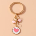 Vista detallada de colgantes de corazón rosa en un llavero de metal dorado elegante - Blanco Rosa