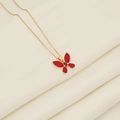 Elegante goldene Schmetterlingshalskette mit roten Edelsteinflügeln auf beigem Stoff - Rot