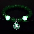 Close-up of luminous green beads and a glowing lotus pendant on a yoga bracelet - 10mm Green Cat's Eye with Green Light