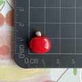 Macro di un ciondolo mela in resina rossa su tappetino graduato da 1,5 cm di larghezza e 1,3 cm - Mela Rossa
