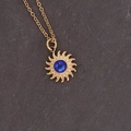 Dettaglio ravvicinato della collana con ciondolo a girasole dorato e gemma blu su pietra - Sole Blu