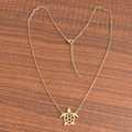 Détail d'un pendentif tortue ajouré sur une chaîne dorée sur une surface en bois - Tortue de mer / Or