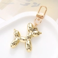 Macro shot of a glossy gold balloon dog keychain with a metallic lobster clasp on a white tray - Gold