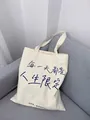 Detail of off-white canvas tote bag with artistic blue calligraphy on a grey sofa - Every Day Is Life Limited