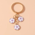 Detailed close-up of three purple and white enamel football charms on a gold keychain link - Purple