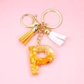 Macro view of golden letter P resin keychain with orange stone chips and colorful tassels - Letter P