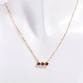 Detalle de tres piedras rojas redondas engastadas en un collar de acero inoxidable dorado - Enero