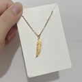 Détail d'un collier pendentif plume dorée présenté sur un support de carte blanche - DN058 Plume Polie