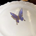 Gros plan d'un clip oreille papillon violet avec monture dorée sur un plat blanc - Ear Cuffs / Violet