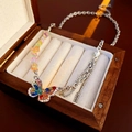 Detalle de un collar de mariposa plateado con cristales de colores en un joyero de madera - Multicolor