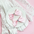 Détail de barrettes à nœuds en satin rose avec cristal en forme de cœur sur dentelle blanche - Rose