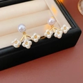 Detalle macro de pendientes de flores doradas con perlas blancas en joyero negro - Pin de Plata 925 / Cobre / Perla Artificial / Dorado