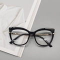 Dettaglio degli occhiali cat-eye neri con accenti metallici dorati su una rivista - Nero Lucido
