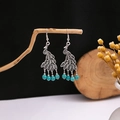Artistic detail of vintage silver peacock drop earrings with turquoise beads on a branch - E2784-7/blue