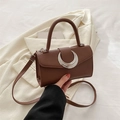 Brown litchi texture crossbody bag with a silver crescent buckle held by hand - Brown