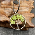 Detailed close-up of tree of life pendant with green natural stones on wood texture - Prehnite