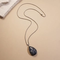 Detailed view of teardrop lapis lazuli pendant on a fine silver chain over warm beige background - Blue