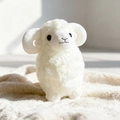 Peluche pecora bianca con corna ricce e morbida pelliccia su un tappeto crema - Bianco