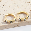 Close-up of gold hoop earrings with evil eye charms and sparkling zircon accents - Black