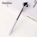 Silver metal ballpoint pen with black obsidian stones and large gemstone top on book - Obsidian