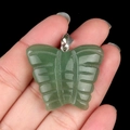 Natural green agate butterfly pendant with silver bail held by hand against black background - Green Aventurine