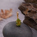 Macro shot of a pear-cut green gemstone pendant in gold setting on a natural pebble - Natural Peridot Water Drop Pendant Gold