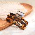 Macro detail of tortoiseshell acetate hair claw clip on a rustic wooden tray - Leopard Print