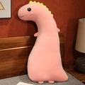 Pink long dinosaur plush pillow with yellow spikes on a bed with soft lighting - Pink Dinosaur