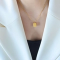 Collana dorata con ciondolo rettangolare inciso in stile minimalista indossata da una modella - Oro